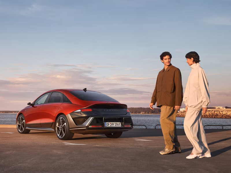 Muškarac i žena prolaze pokraj stražnjeg dijela modela Hyundai IONIQ 6 parkiranog uz obalu.