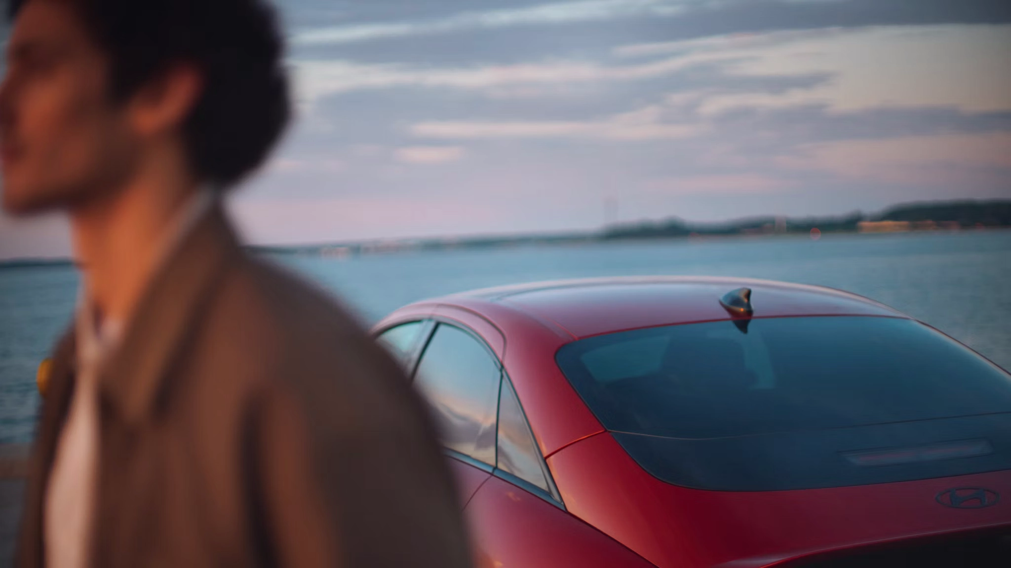 Muškarac prolazi pored crvenog automobila Hyundai IONIQ 6 N Line parkiranog uz obalu.