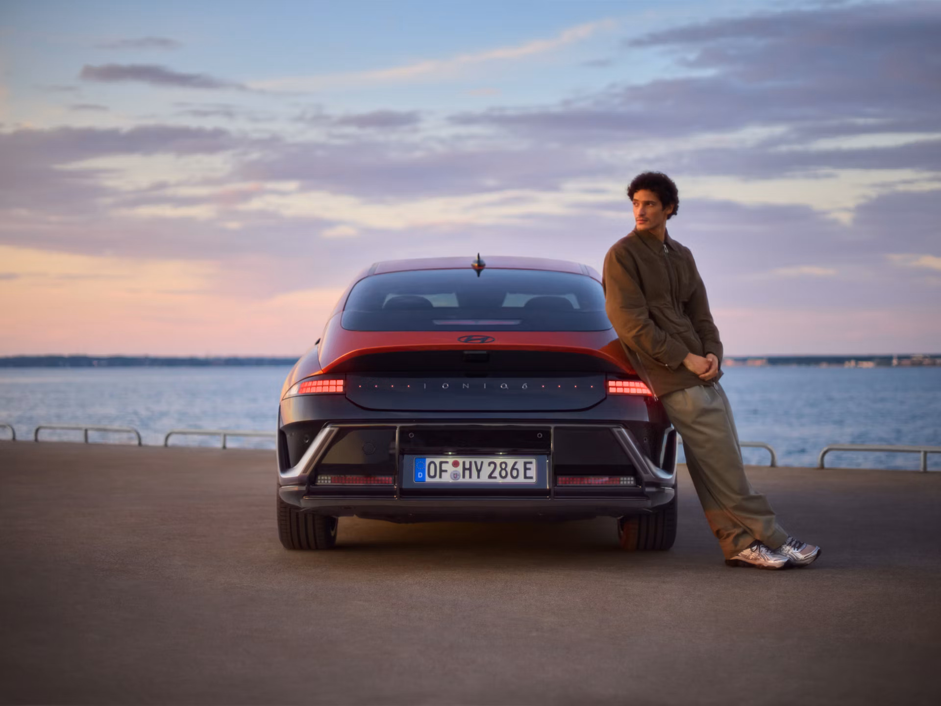 Muškarac oslonjen na bočnu stranu vozila Hyundai IONIQ 6 N Line parkiranog uz obalu.